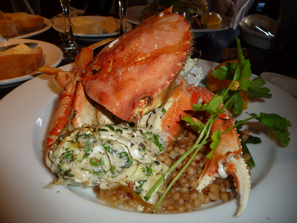 A plated crab dish with greens and grains served at a table set for a seafood meal
